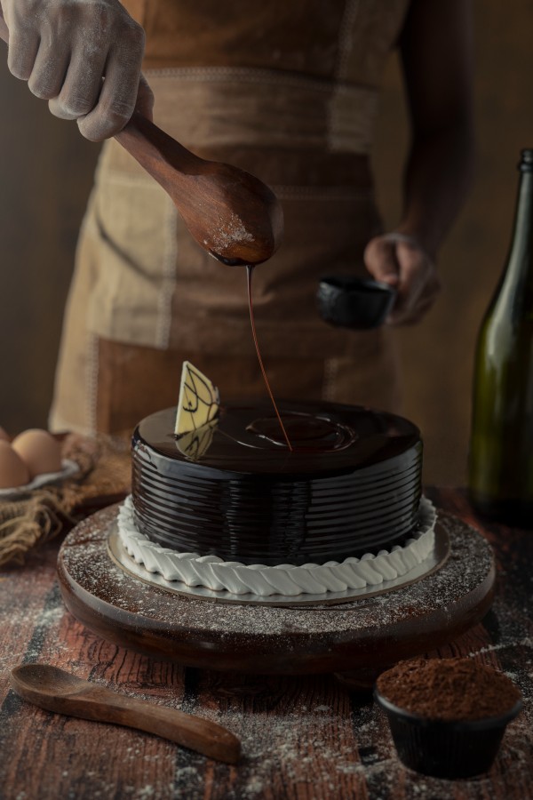 a-man-adding-choclate-on-cake and wooden spoon kept near to it