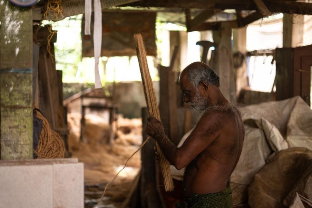 Husk To Rope Man working with coir fibers in a rustic workshop.