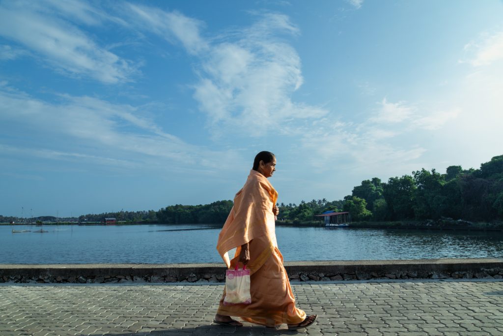 A woman in a flowing elegant saree walks along a seaside path.