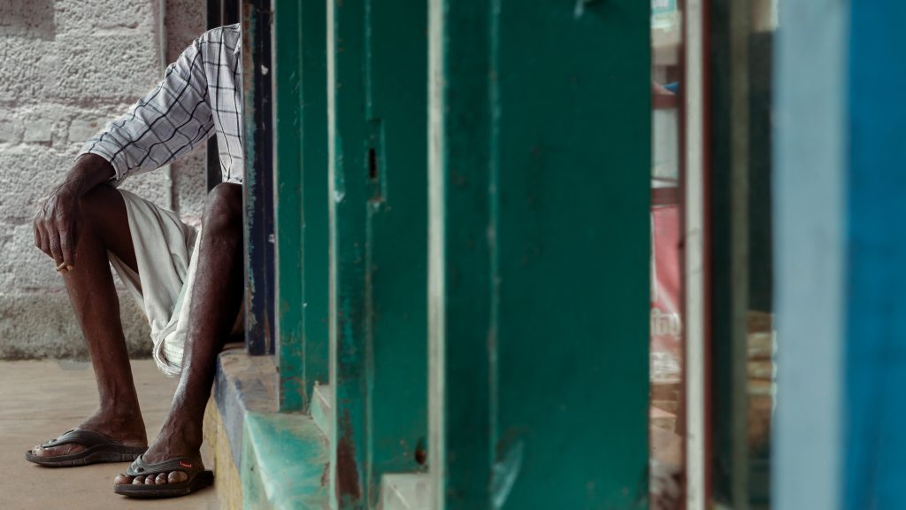 Man sits by a shop, embodying street stillness.