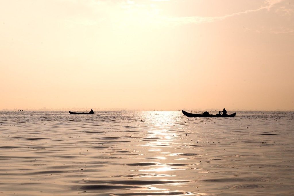 Awakening dawn fishermen's silhouettes rowing boats on a golden sunrise-lit lake.