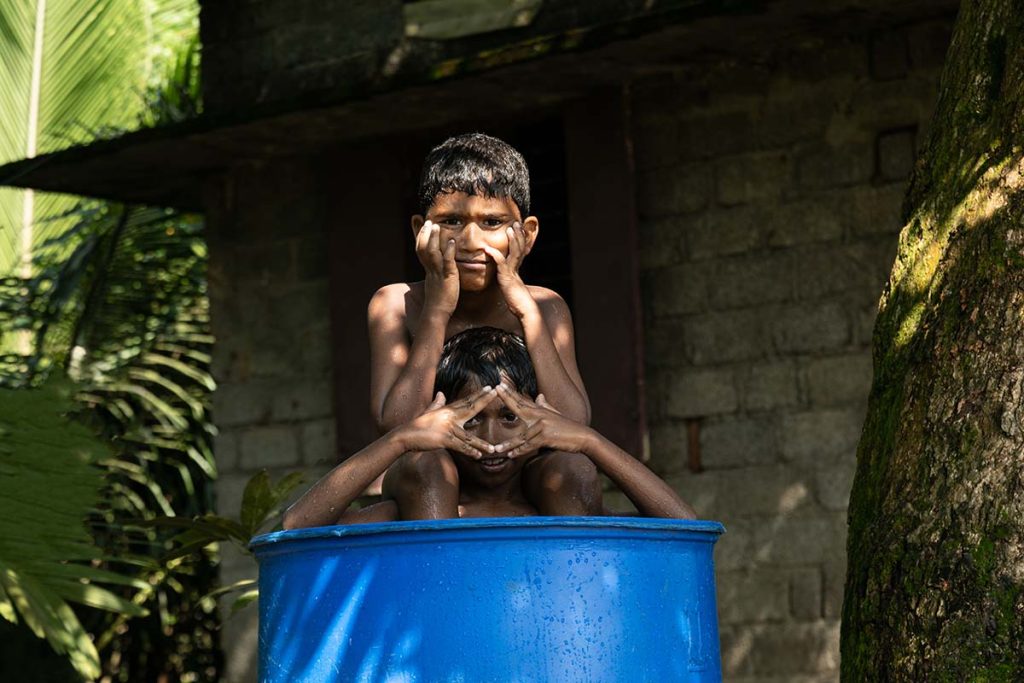 Framed Eyes Two boys gesture with their hands inside a blue barrel.