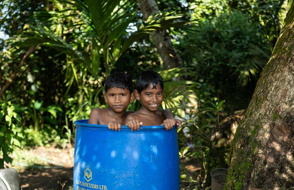 Joyful Bond Two boys smiling while bathing in a blue barrel outdoors.