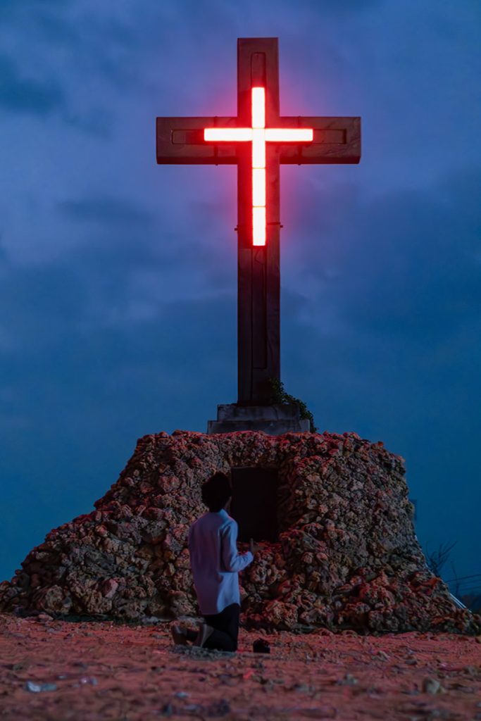 Luminous Reverence  A man kneeling in front of a cross.