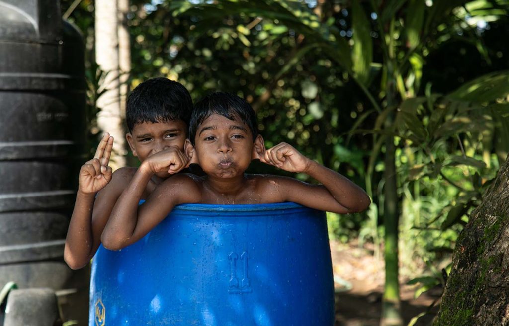 Playful Moments Two boys playfully posing inside a blue barrel.