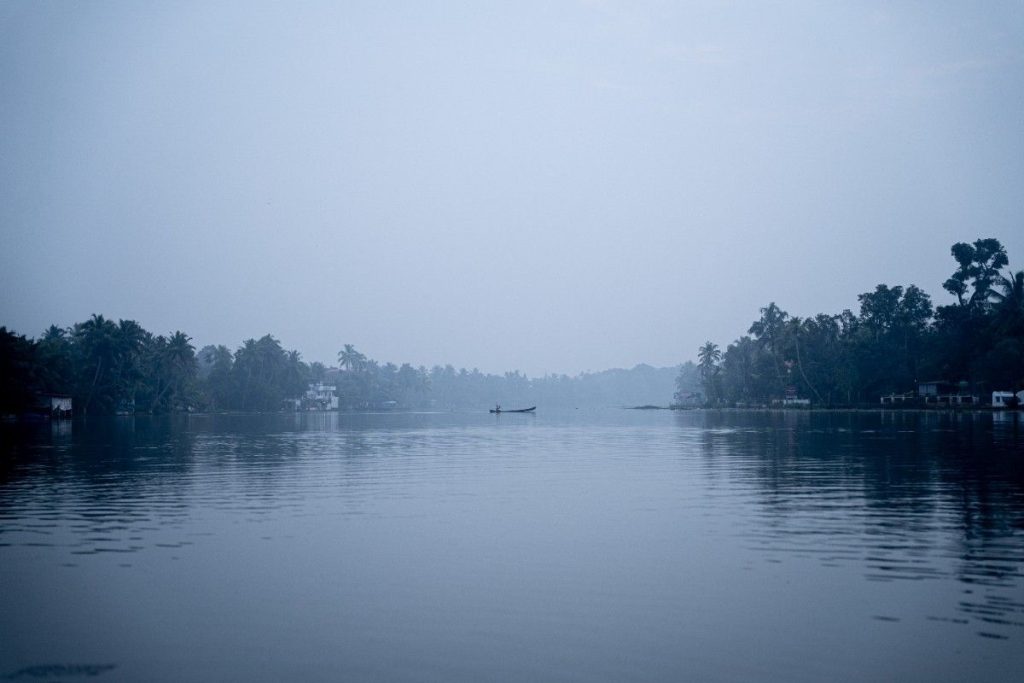 In quiet depths a village man paddling a canoe on misty backwaters.