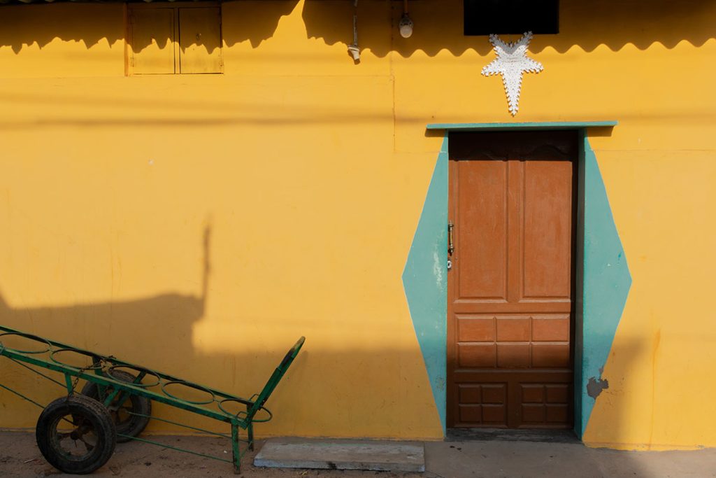 sunlit facade, a yellow wall with wooden door.