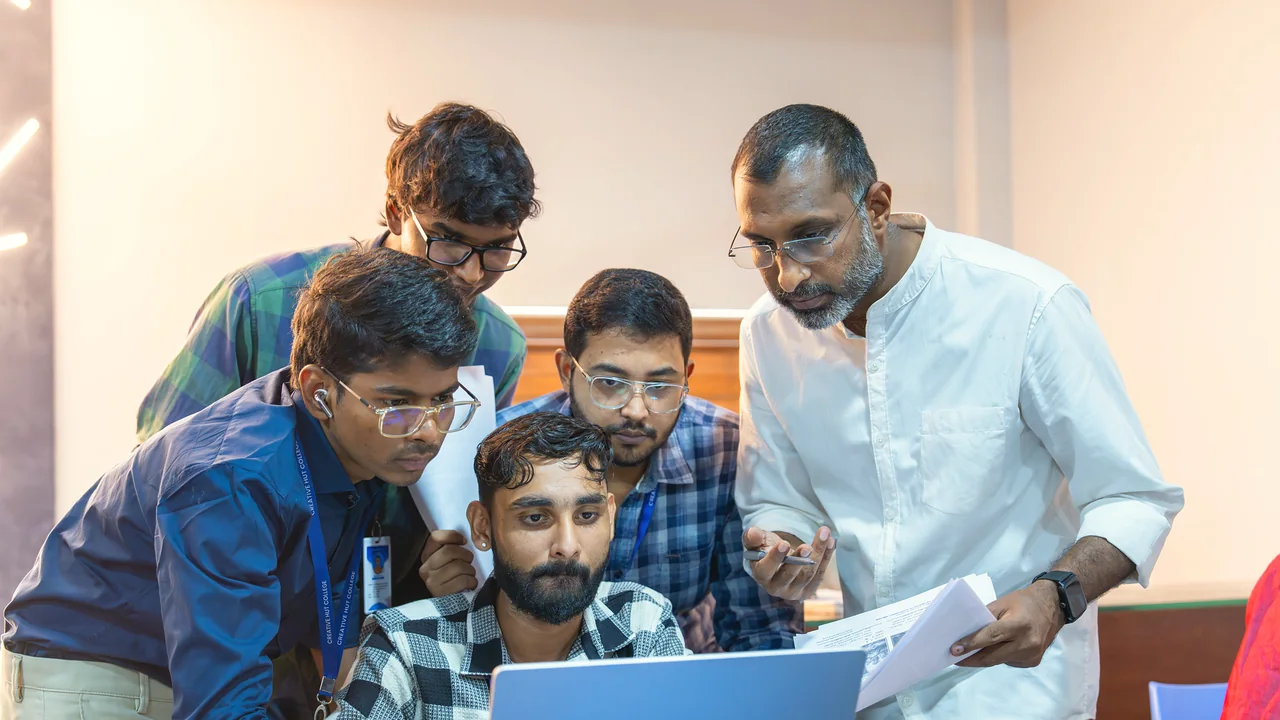 Creative Hut Academy students and a faculty member reviewing work together on a laptop