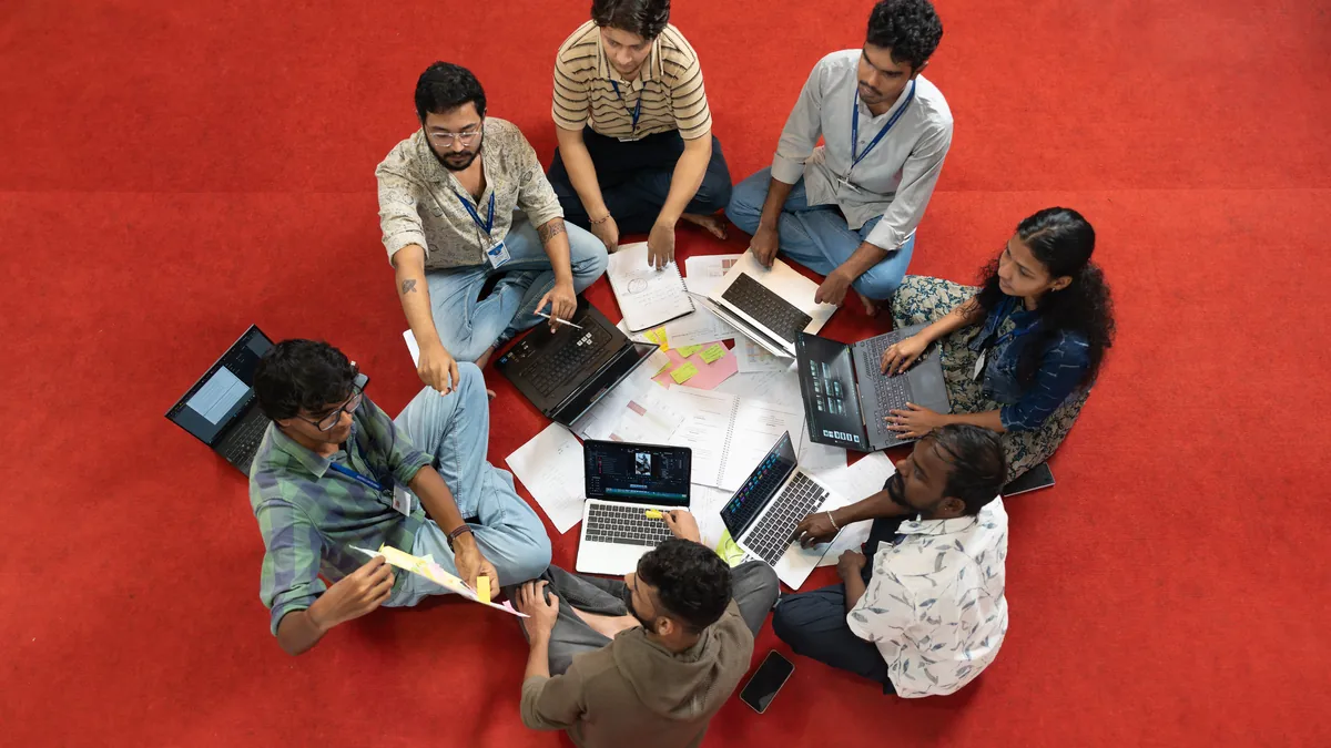 Overhead view of film students collaborating with laptops on a red floor at Creative Hut Academy