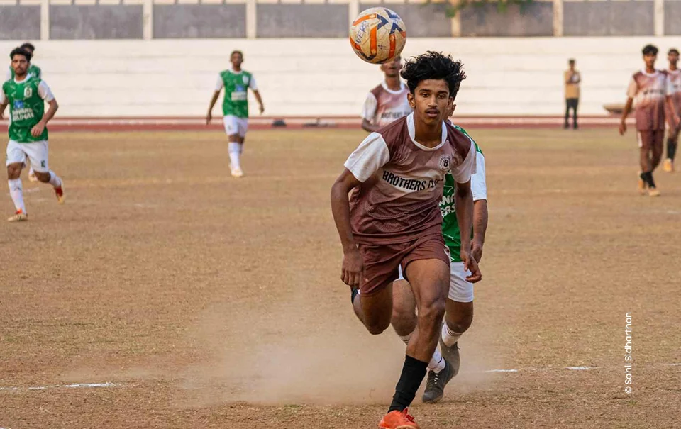 Footballer in brown jersey chasing the ball across a dusty pitch, sports photograph by Sahil Sidharthan, Creative Hut Academy