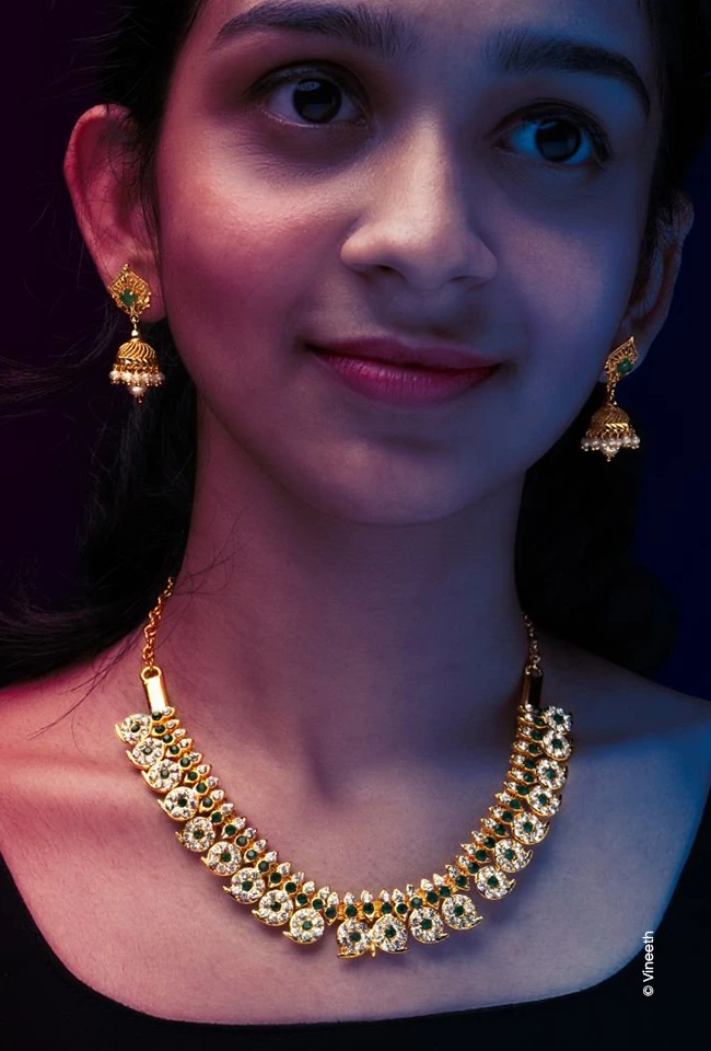 Girl in a gold necklace and jhumka earrings smiling at the camera, advertising photograph by Vineeth, Creative Hut Academy