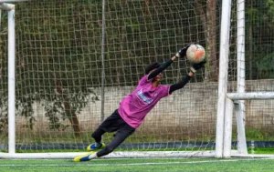 Goalkeeper in pink diving to push the ball away, sports photograph by Ajinlal S, Creative Hut Academy