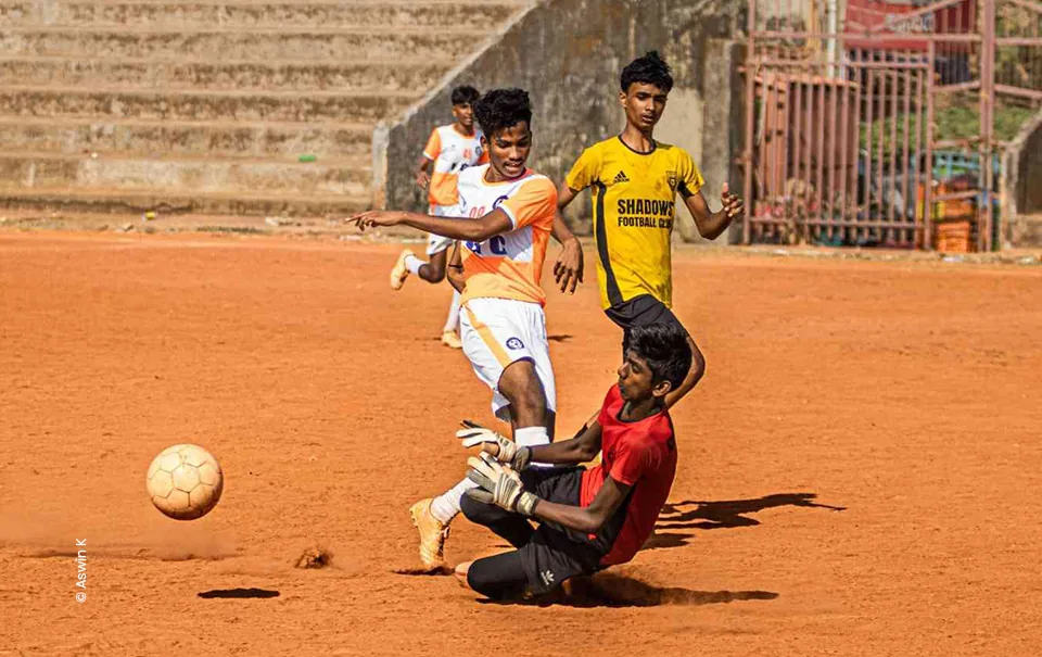 Goalkeeper sliding in to challenge a striker on a clay pitch, sports photograph by Aswin K, Creative Hut Academy