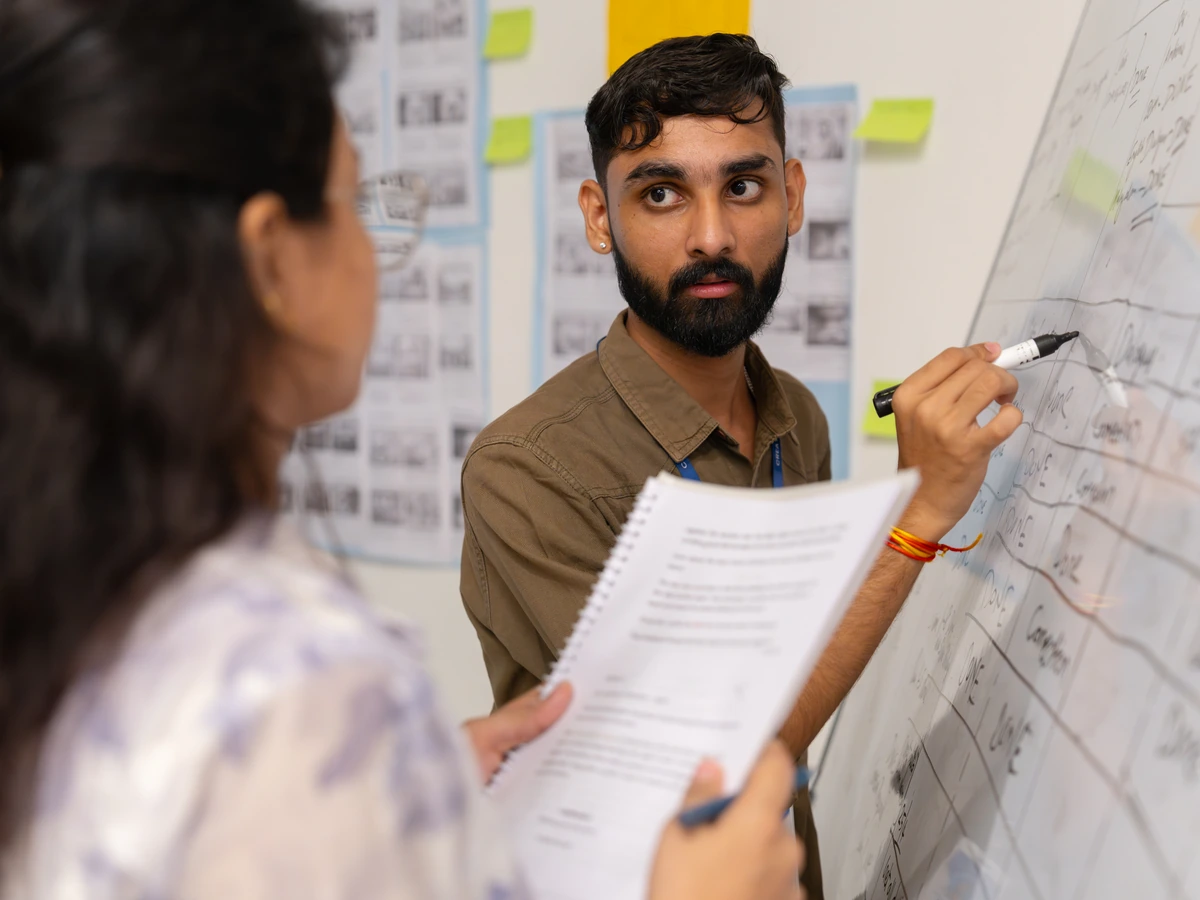 Film school student marking a storyboard on a whiteboard while a classmate holds the script